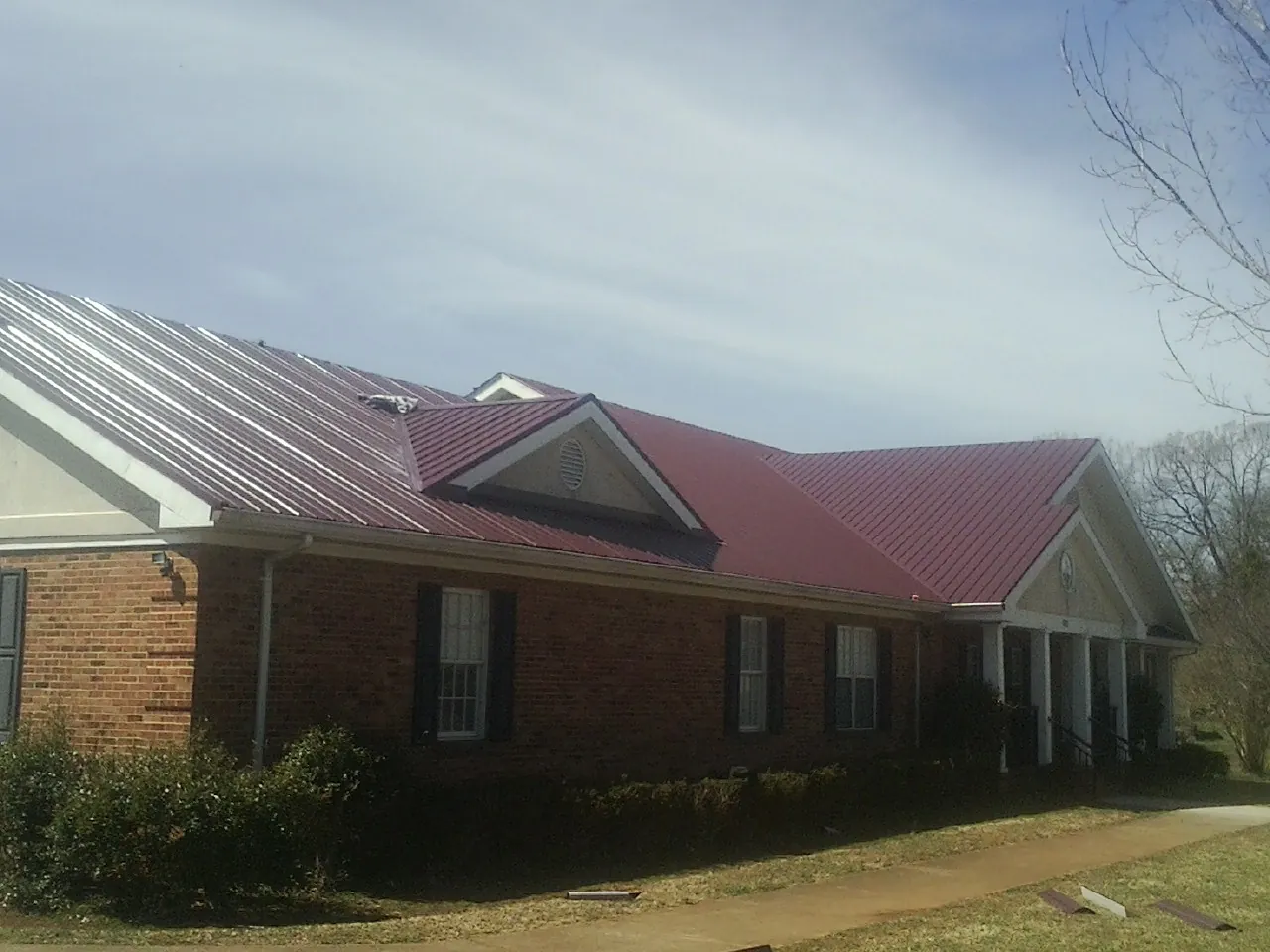 Red metal roof with gabled entries on a long brick building, from a Hail Damage Roof Repair job in Pine Level