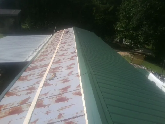 Old rusted panels beside newly installed green metal roofing — Wind Damage Roof Repair by Roofing Brothers in Pine Level