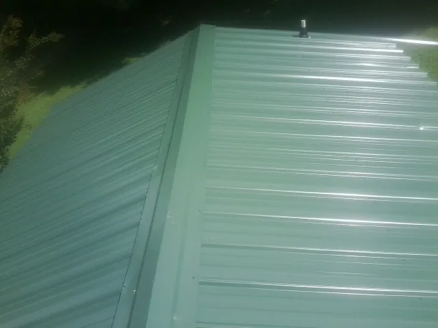 New green metal panels meeting at the ridge of a roof — Flat Roof Repair work by our crew in Pine Level