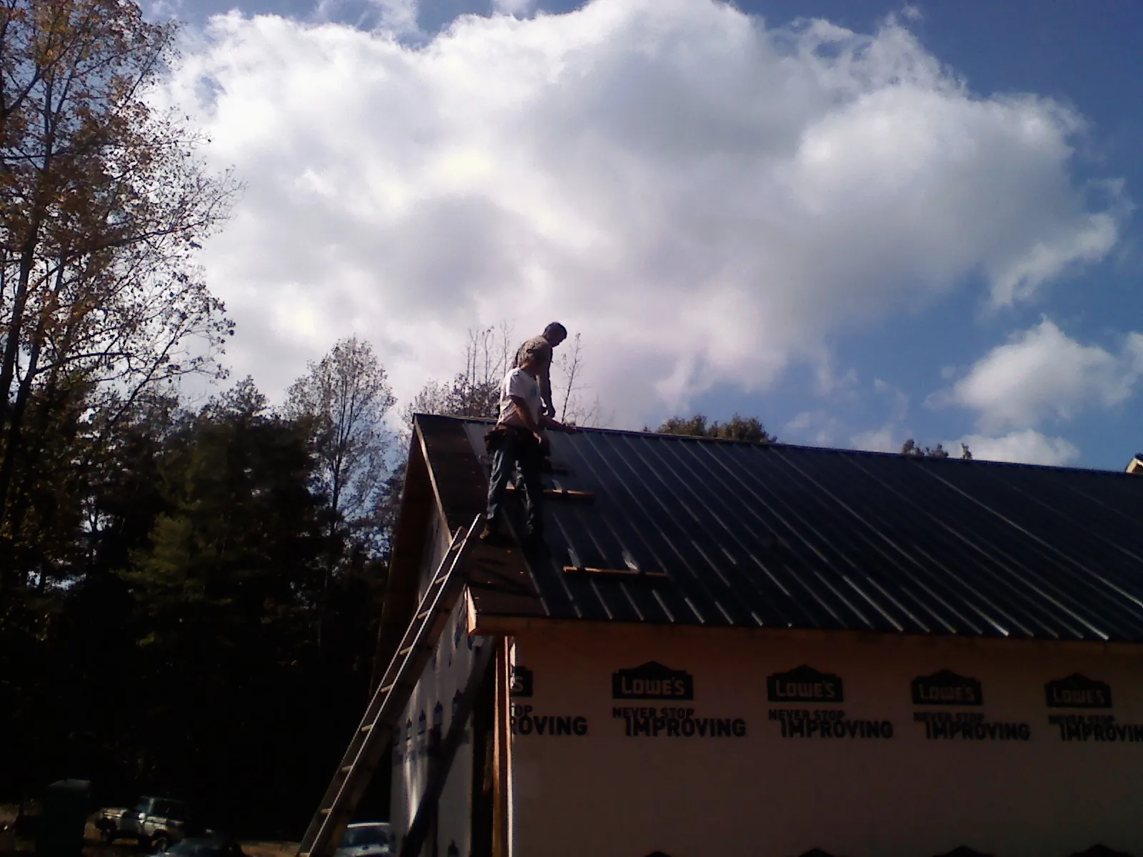 Roofer fastening dark metal panels high against a cloudy sky, from a Roof Inspection job in Pine Level