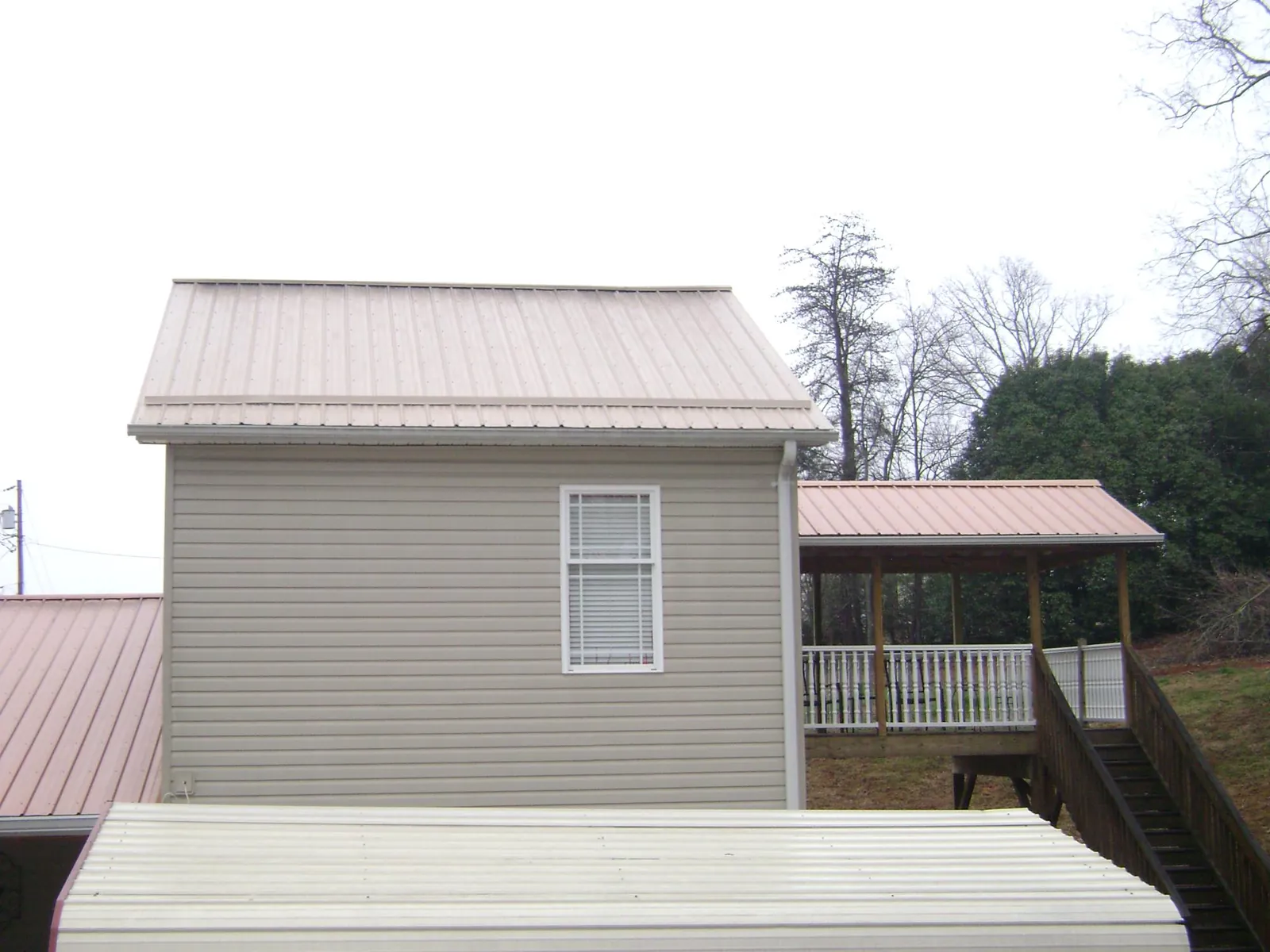 Tan metal roofs on a two story addition and attached porch, from a Roof Replacement job in Pine Level